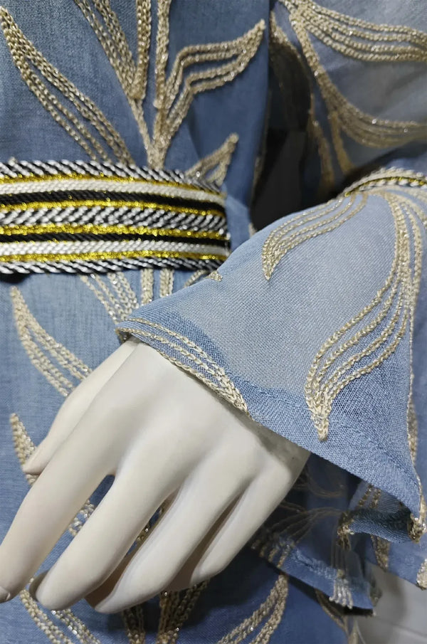 Extreme close-up of the light blue Kitala Kaftan's sheer fabric, metallic gold leaf embroidery, and braided jeweled belt details.