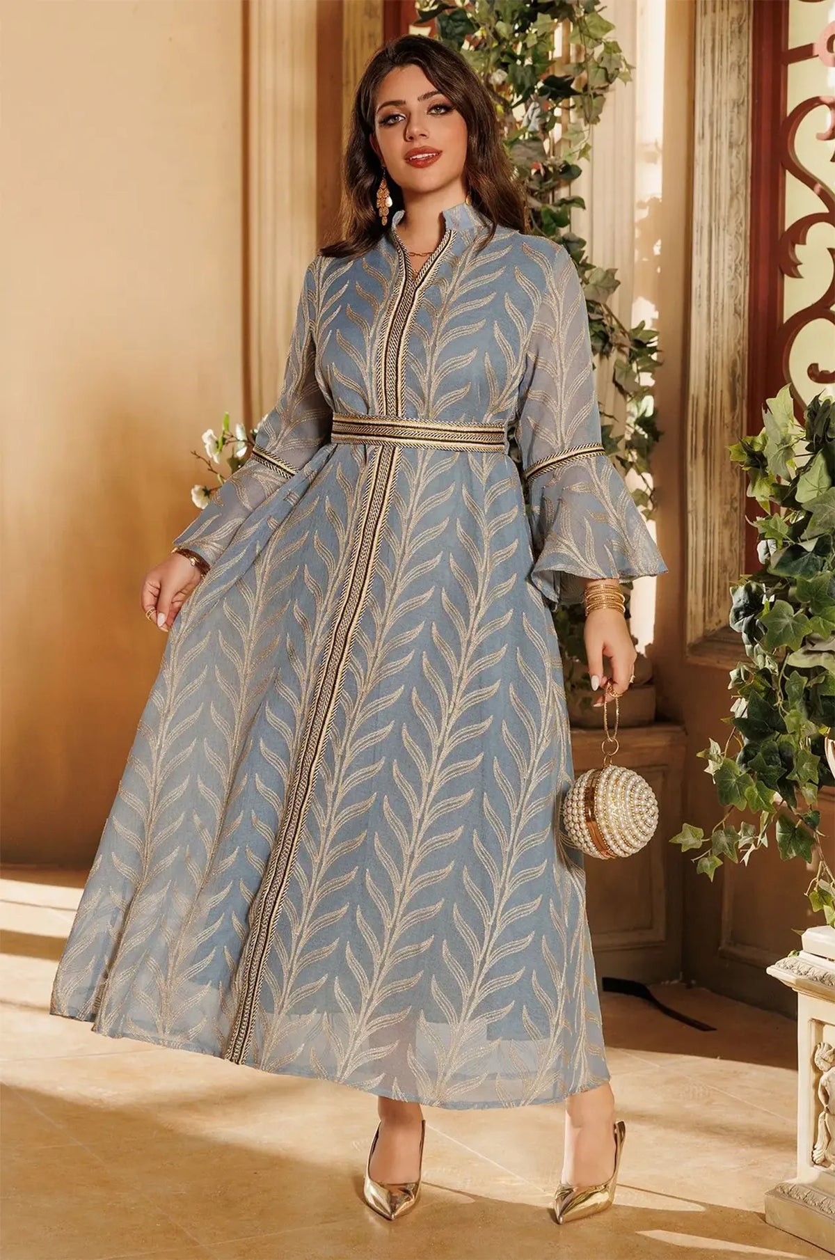Elegant three-quarter view of the light blue Kitala Kaftan by Naylara, featuring gold leaf embroidery and accessorized with a decorative pearl handbag.