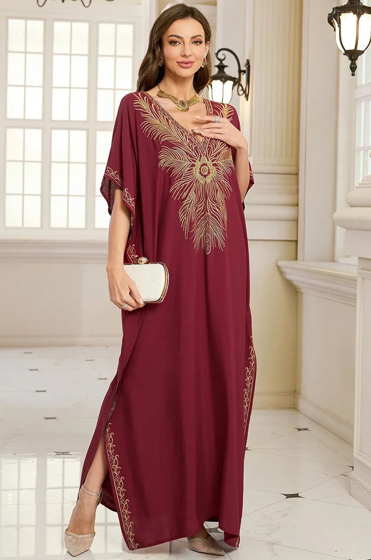 Naylara Laurel red Moroccan kaftan styled with white clutch and gold jewelry — 3/4 palace view