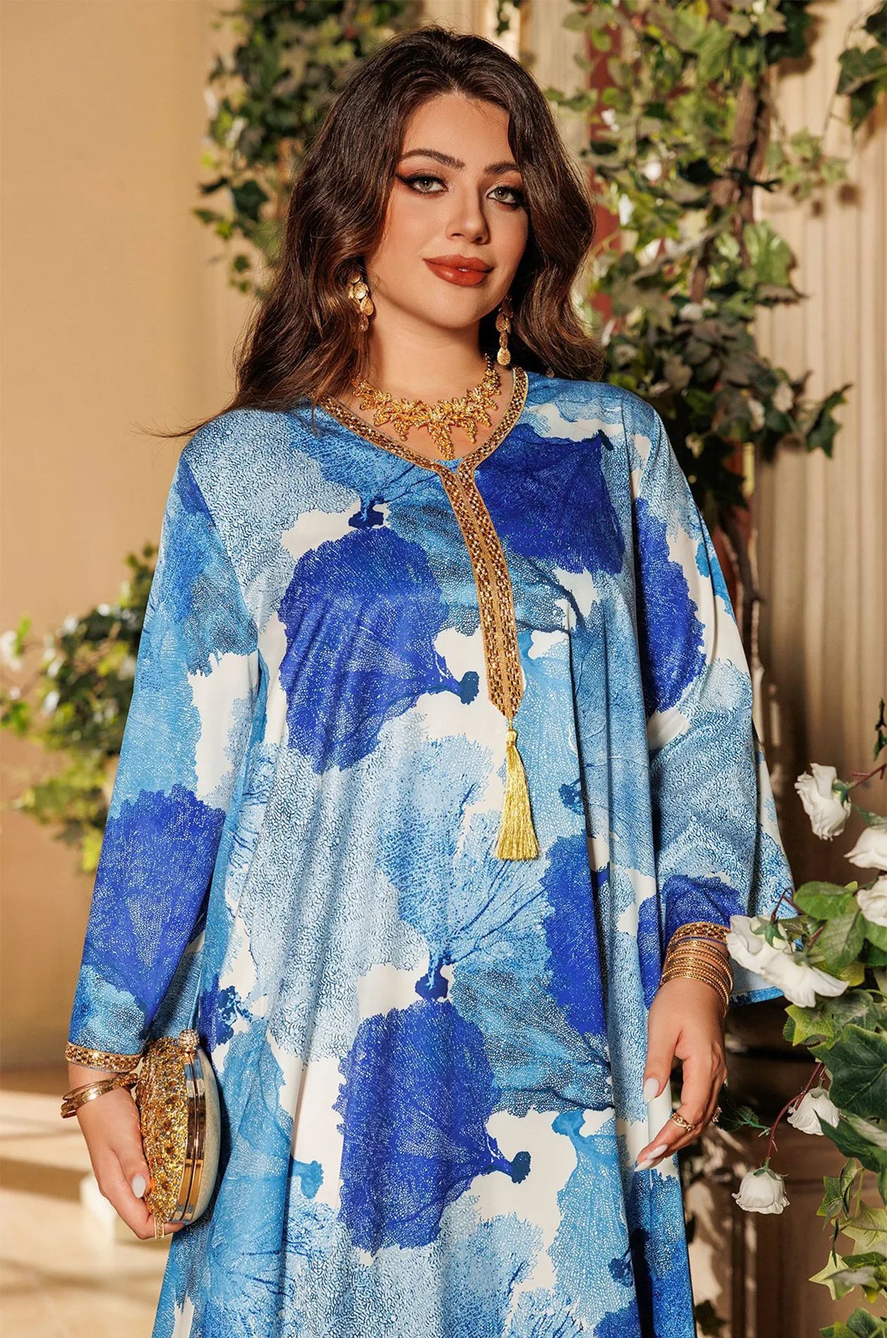 Close-up of the Navae blue tropical print kaftan paired with a gold evening clutch and jewelry.