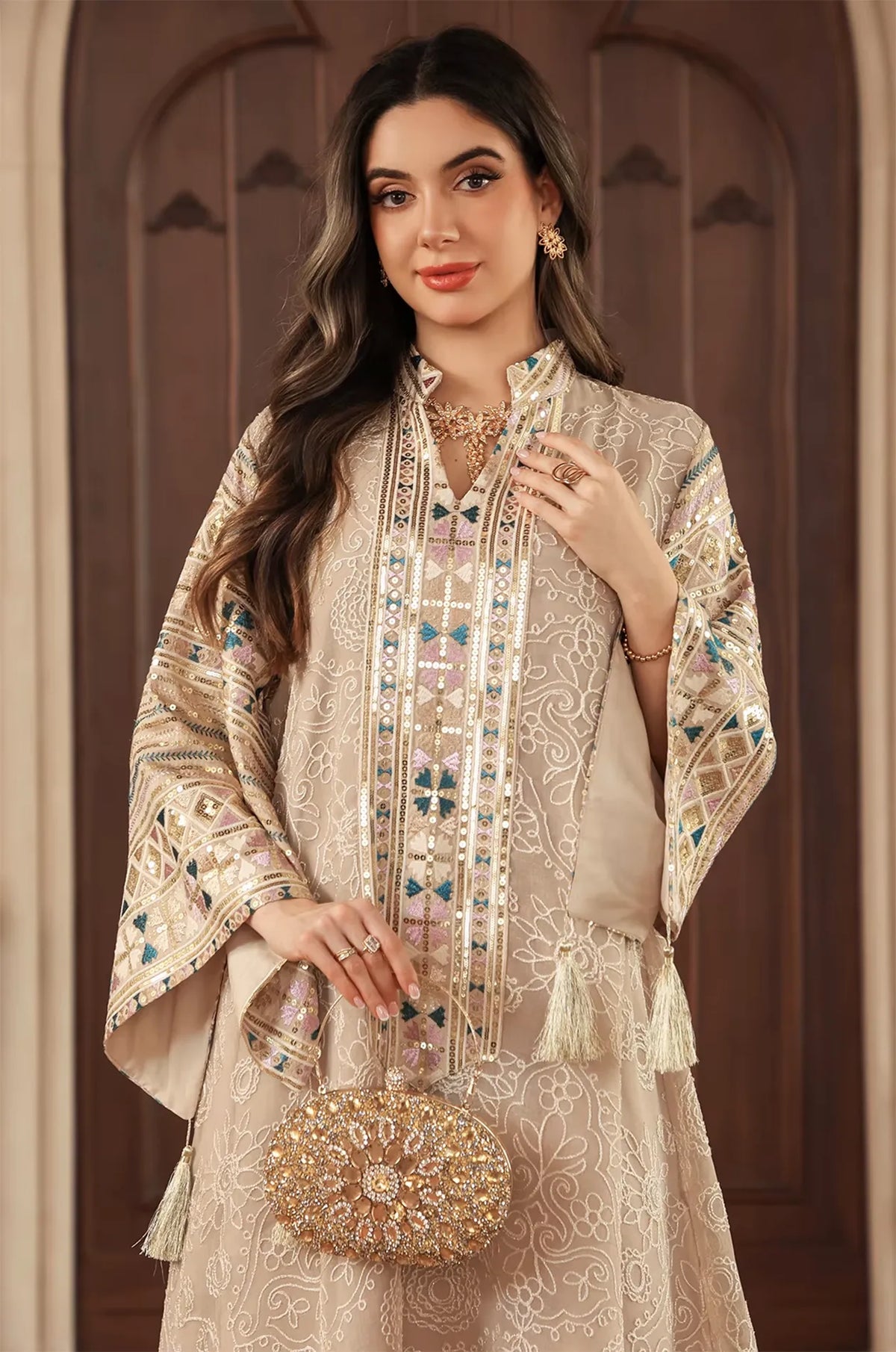 Half-body view of the apricot beige Orla kaftan styled with a gold clutch and V-neck sequin detailing.