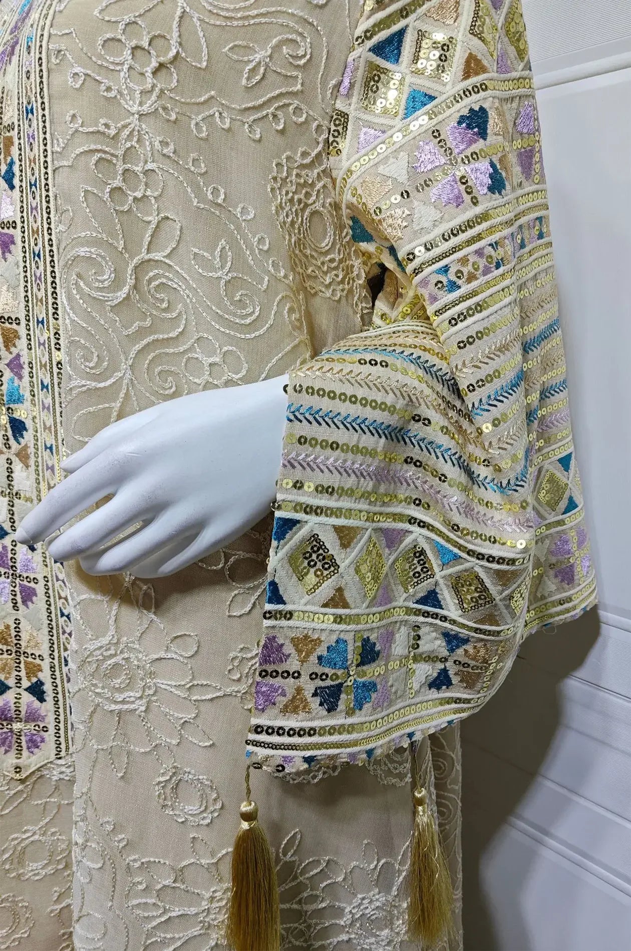 Macro detail of the Orla apricot beige kaftan sleeve featuring metallic geometric sequins and tassels.