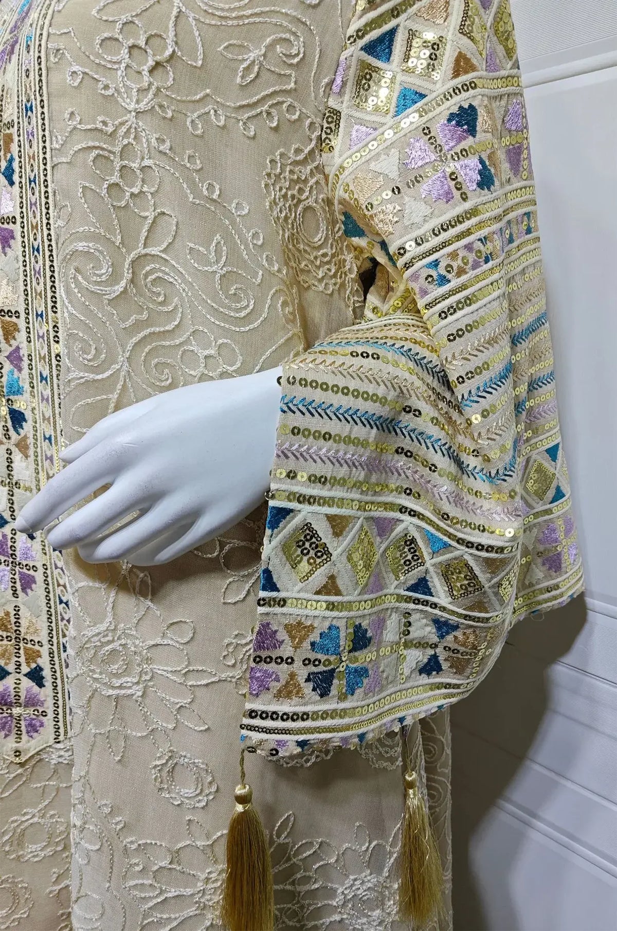 Macro detail of the Orla apricot beige kaftan sleeve featuring metallic geometric sequins and tassels.
