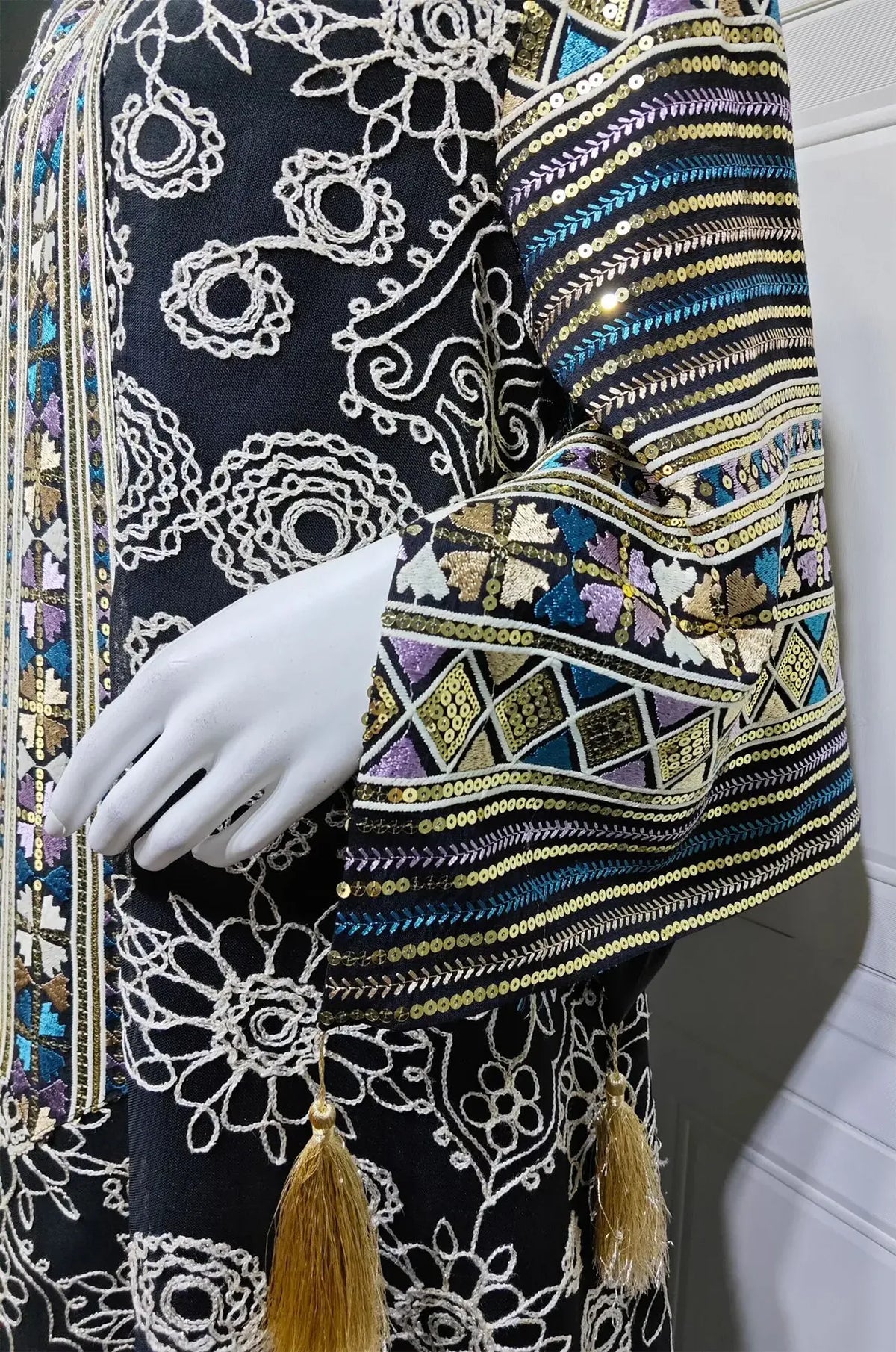 Macro detail of the Orla black kaftan’s bell sleeves featuring colorful sequins, geometric embroidery, and luxury silk tassels.