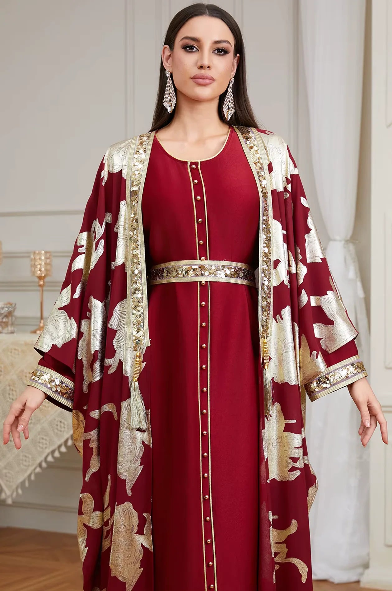 Close-up view of the Naylara Puppis red and gold kaftan luxe showing the intricate sequined trim, gold buttons, and tassel accents.