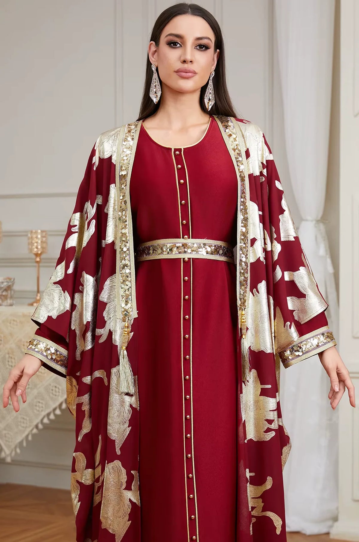 Close-up view of the Naylara Puppis red and gold kaftan luxe showing the intricate sequined trim, gold buttons, and tassel accents.