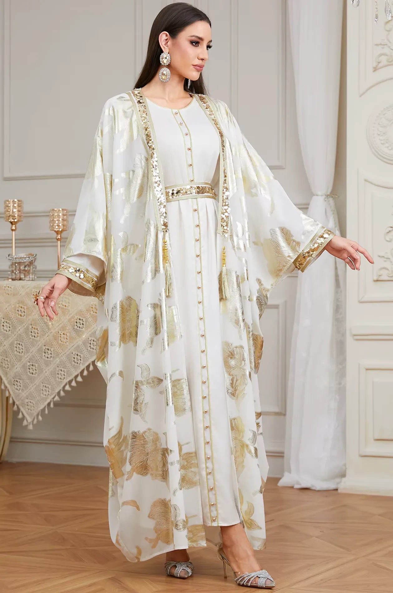 A full-length view of the Naylara Puppis white luxe kaftan featuring intricate gold floral patterns and shimmering sequined borders.