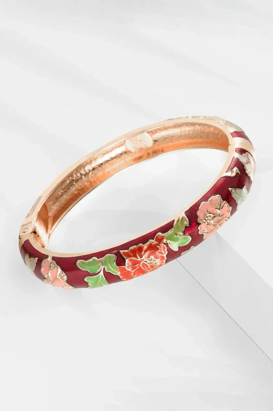 Vintage style red enamel bracelet with floral motifs laying on white surface.