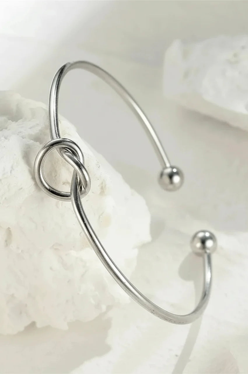 Artistic shot of silver knot bangle displayed on white textured stone.