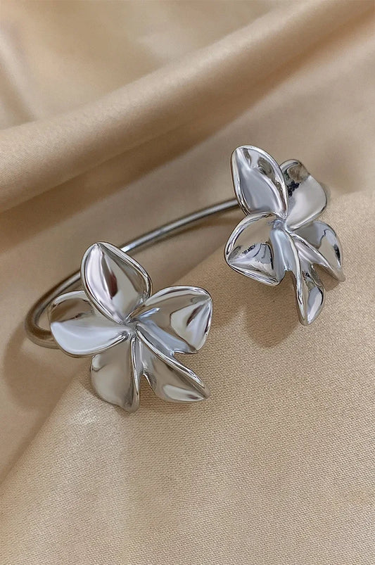 Silver flower bangle bracelet displayed on soft champagne silk fabric.