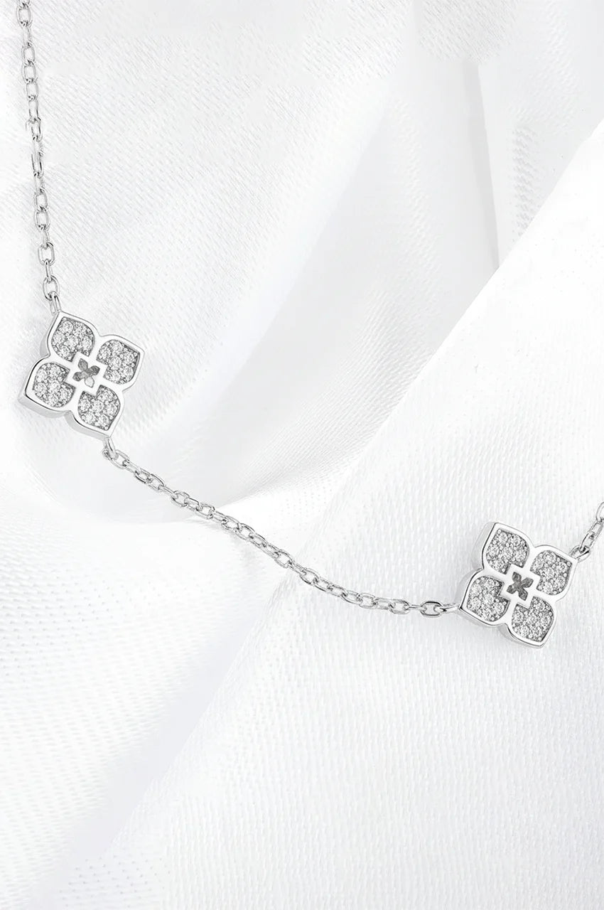Silver four-petal flower necklace draped on soft white fabric texture