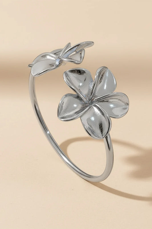 Silver open cuff bracelet with floral motif standing on beige background.