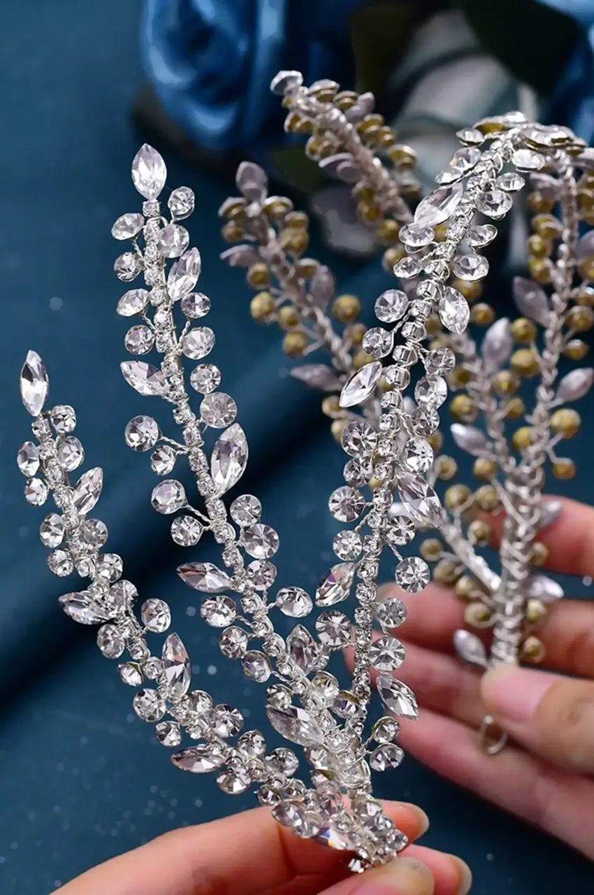 Hand holding the Silver-Tone Crystal Headpiece, showing the flexible silver wire frame and the intricate golden/silver bead accents on the backing.