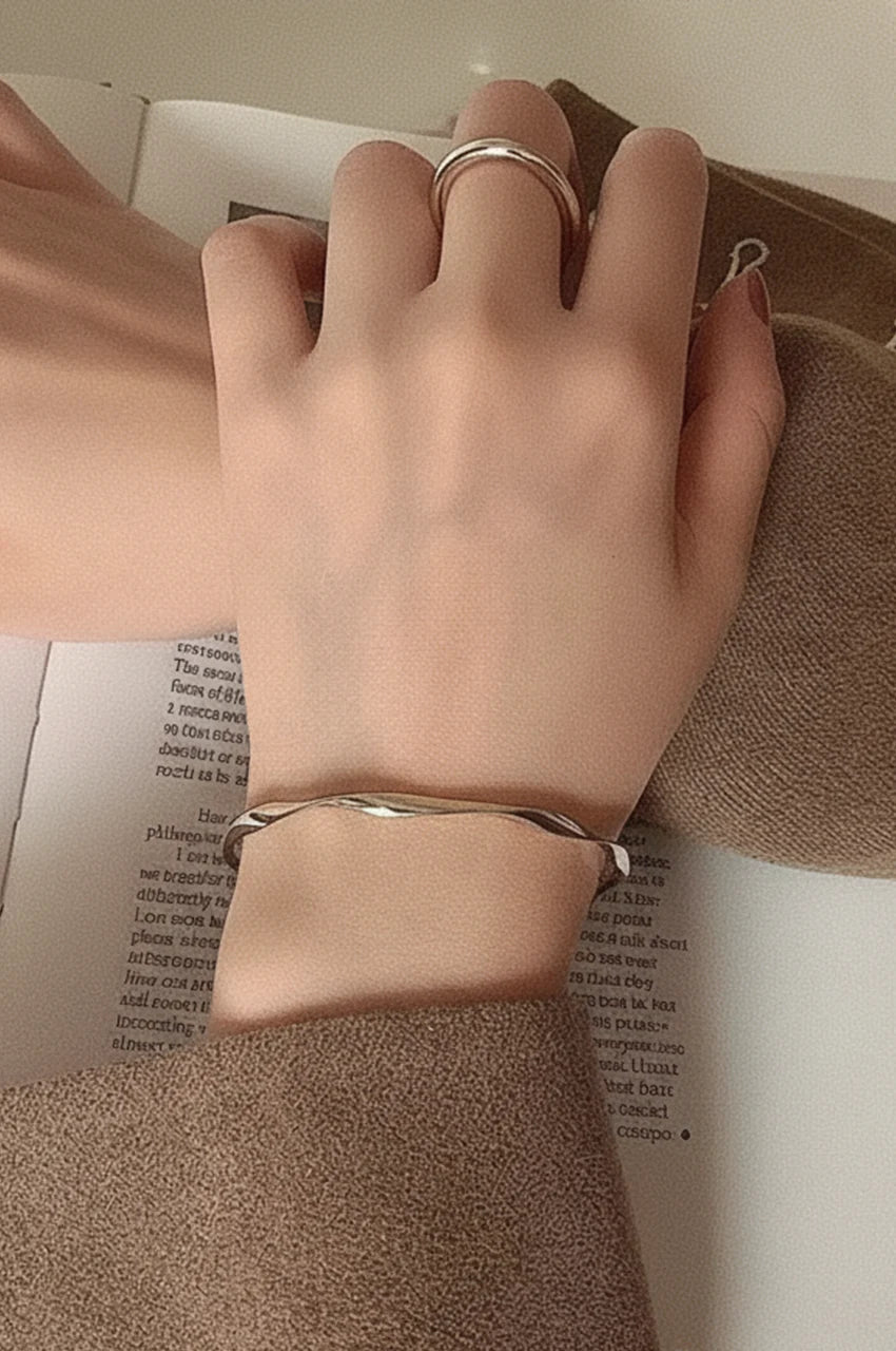 Woman wearing minimalist silver wave bangle on wrist.