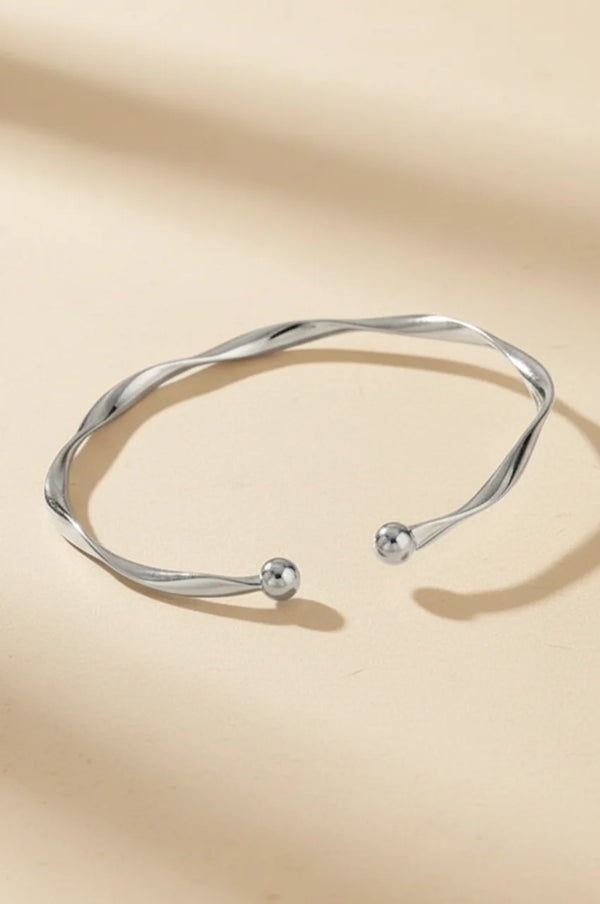 Polished silver wave bangle with ball ends on beige background.