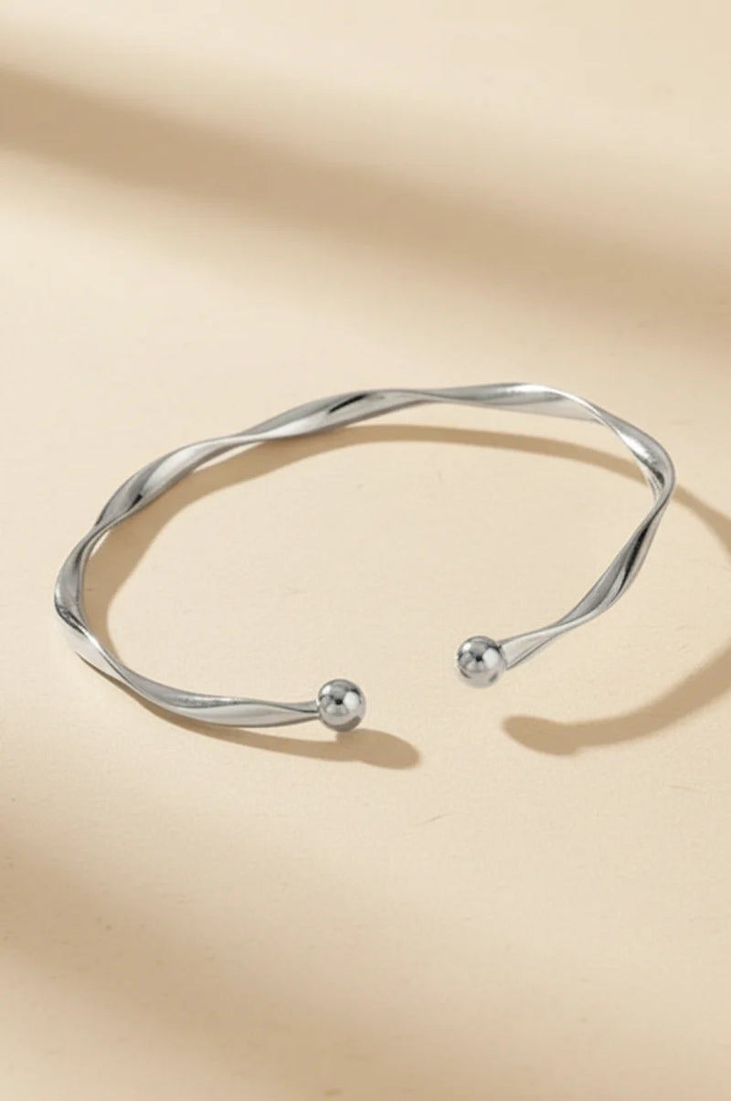 Polished silver wave bangle with ball ends on beige background.