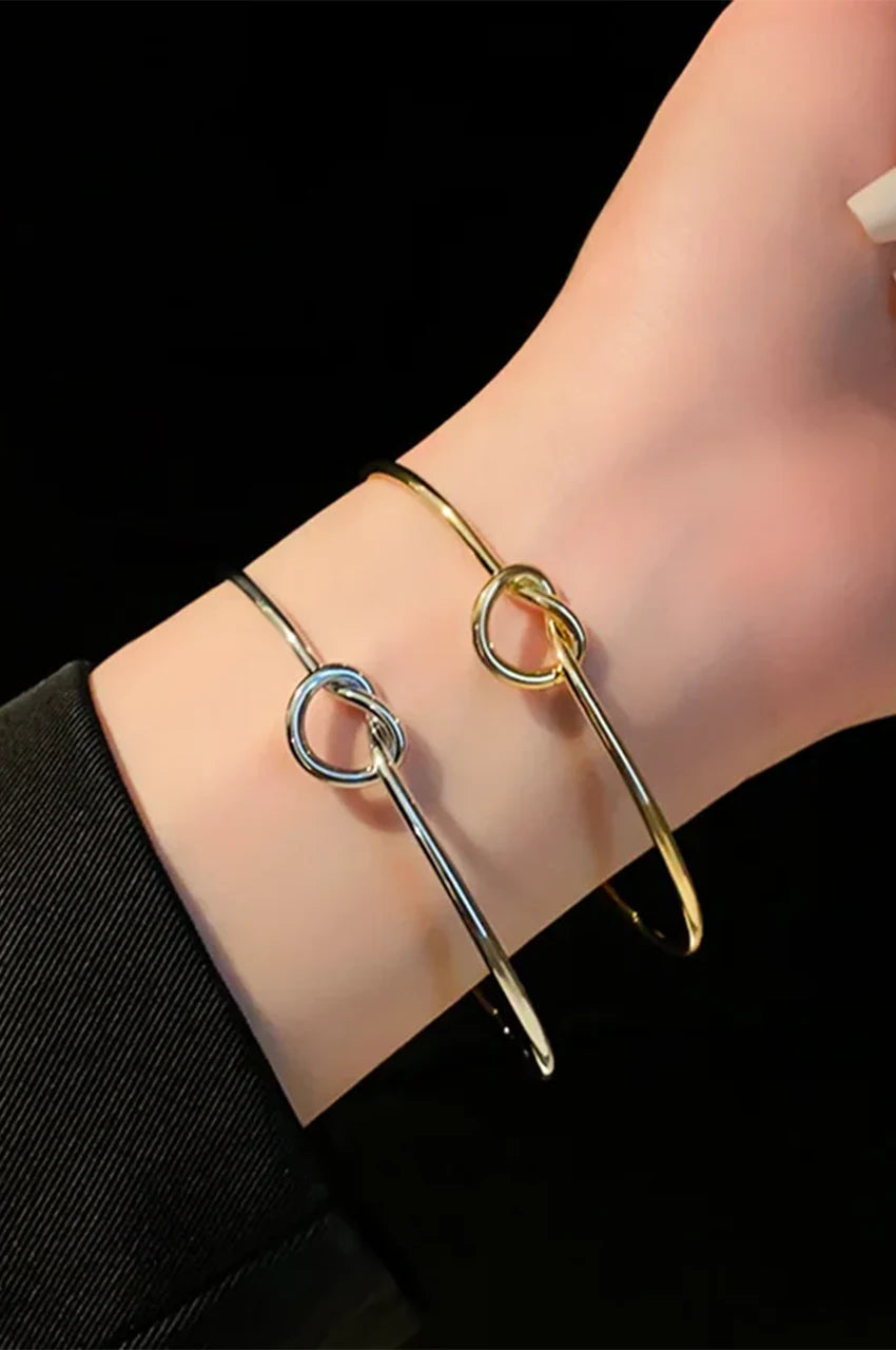 Woman wearing gold and silver knot bangles stacked on wrist.