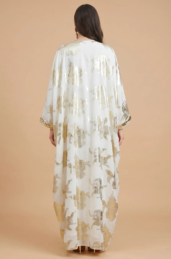 The back view of the white Puppis luxe kaftan showing the elegant drape of the gold floral printed cape overlay.