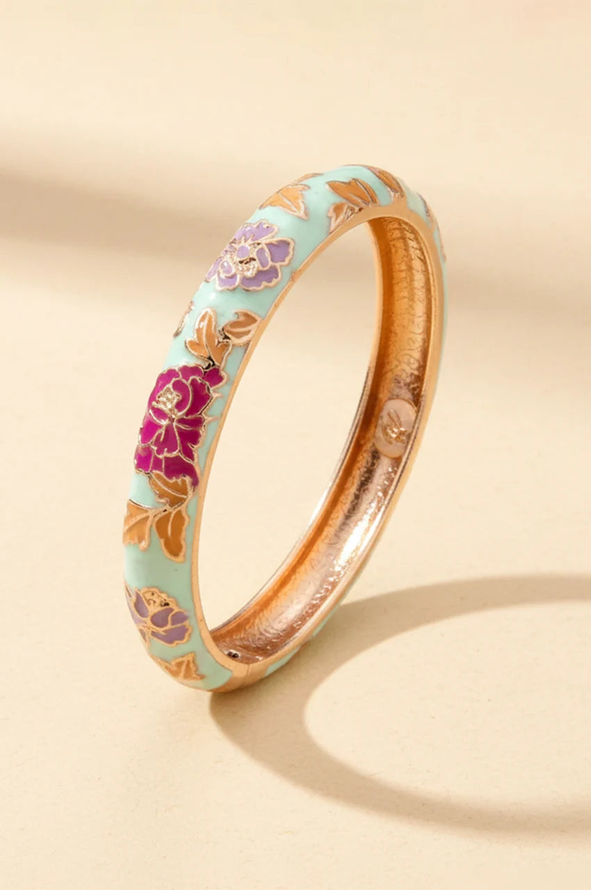 White and mint tint enamel bangle with purple flowers standing on beige background.
