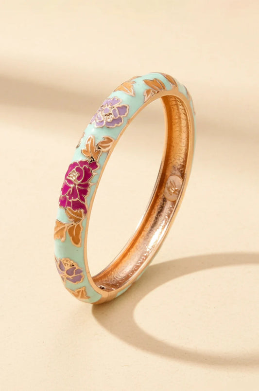 White and mint tint enamel bangle with purple flowers standing on beige background.