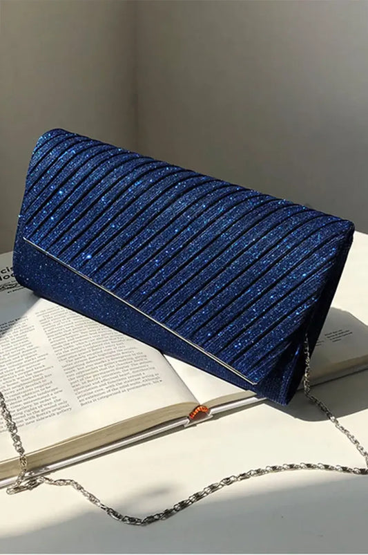 Angled profile view of night blue glitter clutch on a white surface, showcasing the diagonal pleated structure and silver chain.