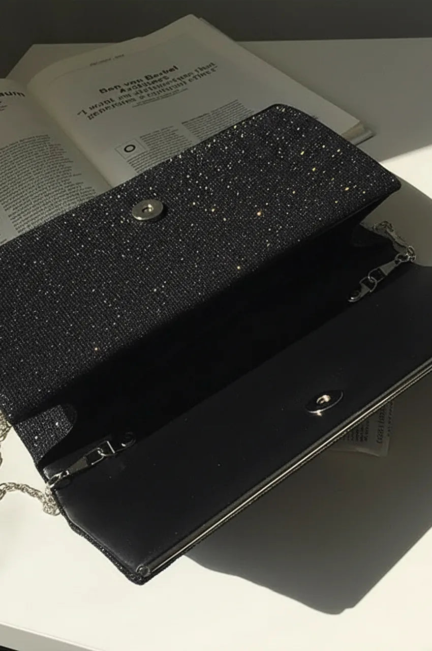 Interior view of open black clutch bag revealing black fabric lining, internal pocket, and chain clips.