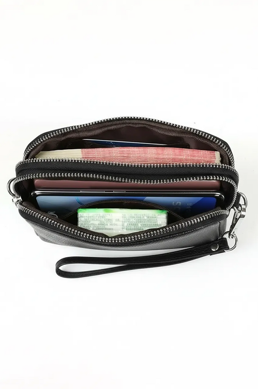 Top view inside open black leather clutch showing dual zippered compartments holding cash, phone, and tissues.