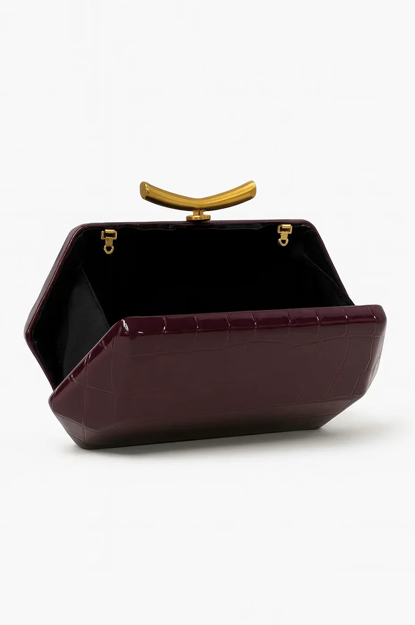 Interior view of open burgundy hard-shell clutch showing black fabric lining, side gussets, and gold hinge details.