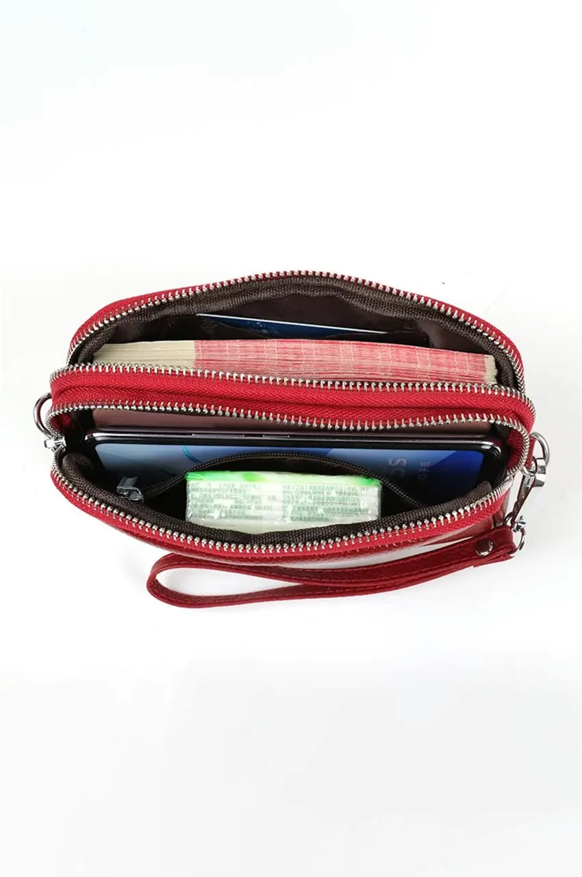 Top view inside open red leather clutch showing two zippered compartments organized with cash, smartphone, and essentials.