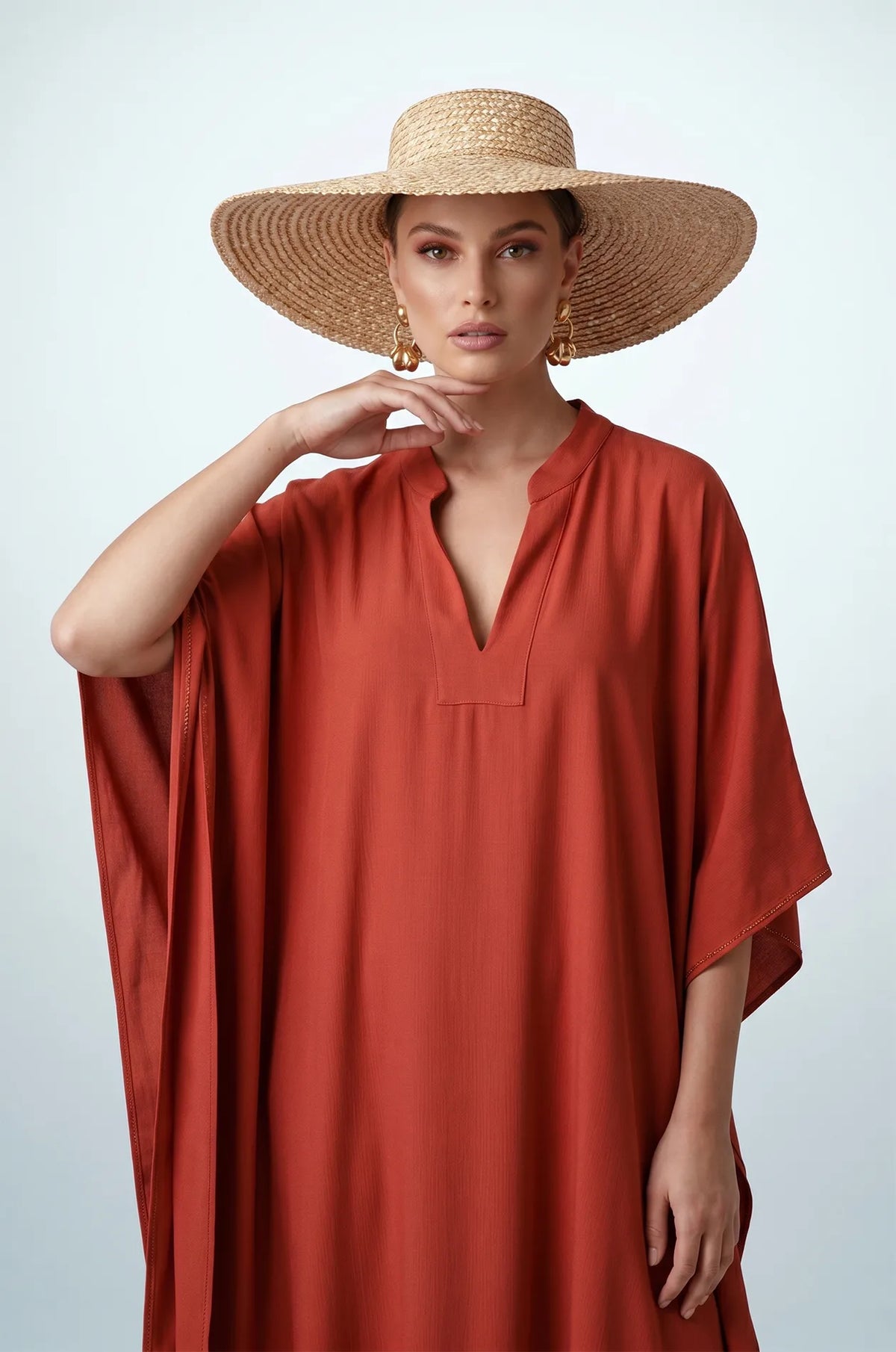 Woman in terracotta orange plain kaftan styled with wide-brim straw hat