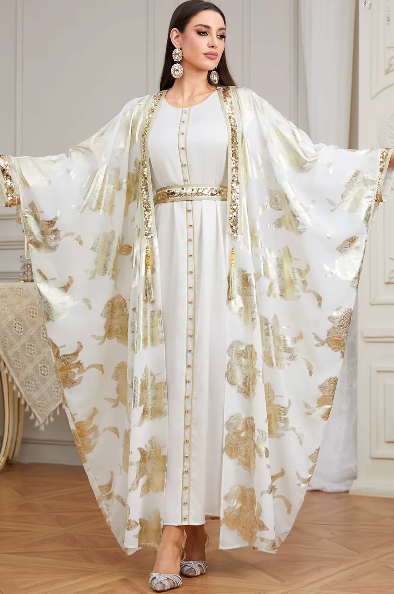 Full-length shot of the white Puppis kaftan luxe with arms extended to display the dramatic butterfly cape wingspan and floral gold motifs.