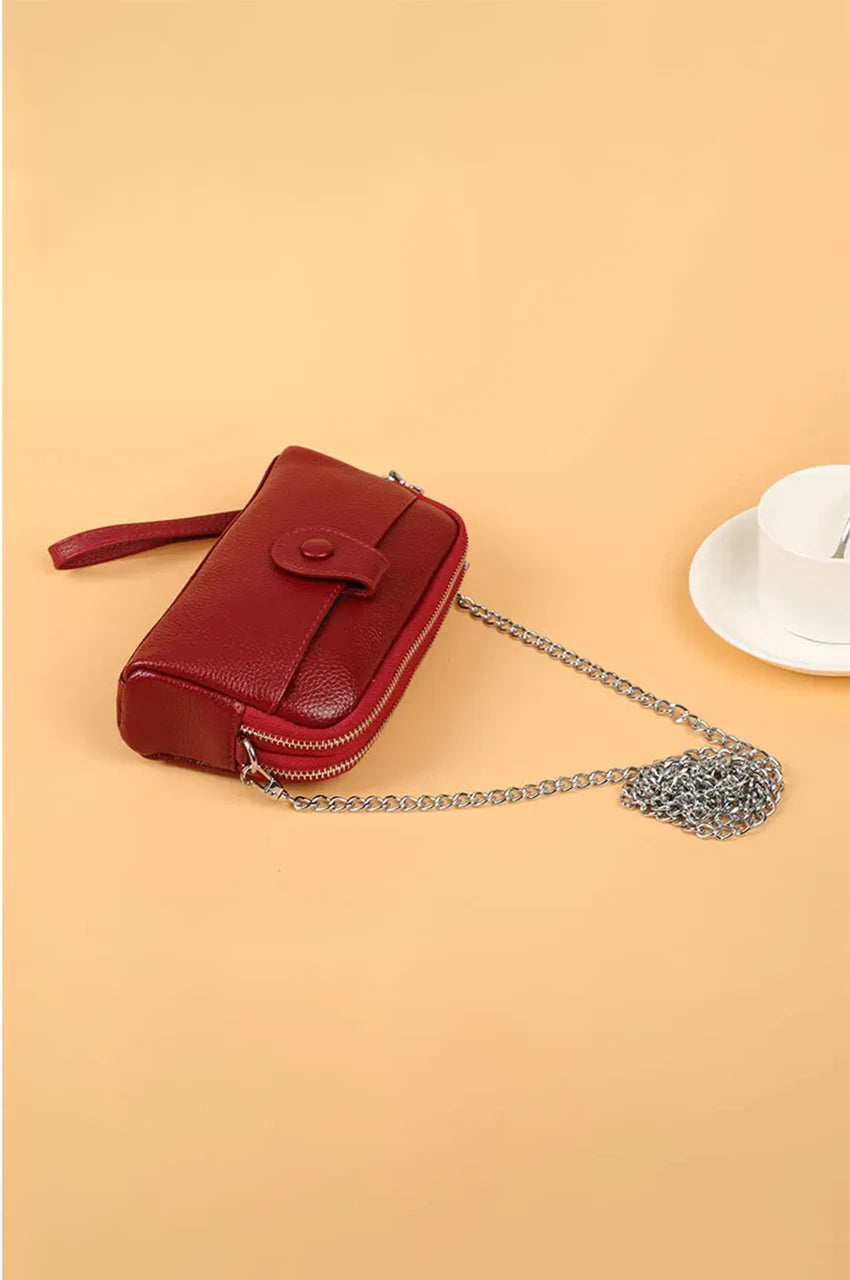 Angled side view of red leather wristlet wallet showing depth, texture, and the detachable silver chain strap.