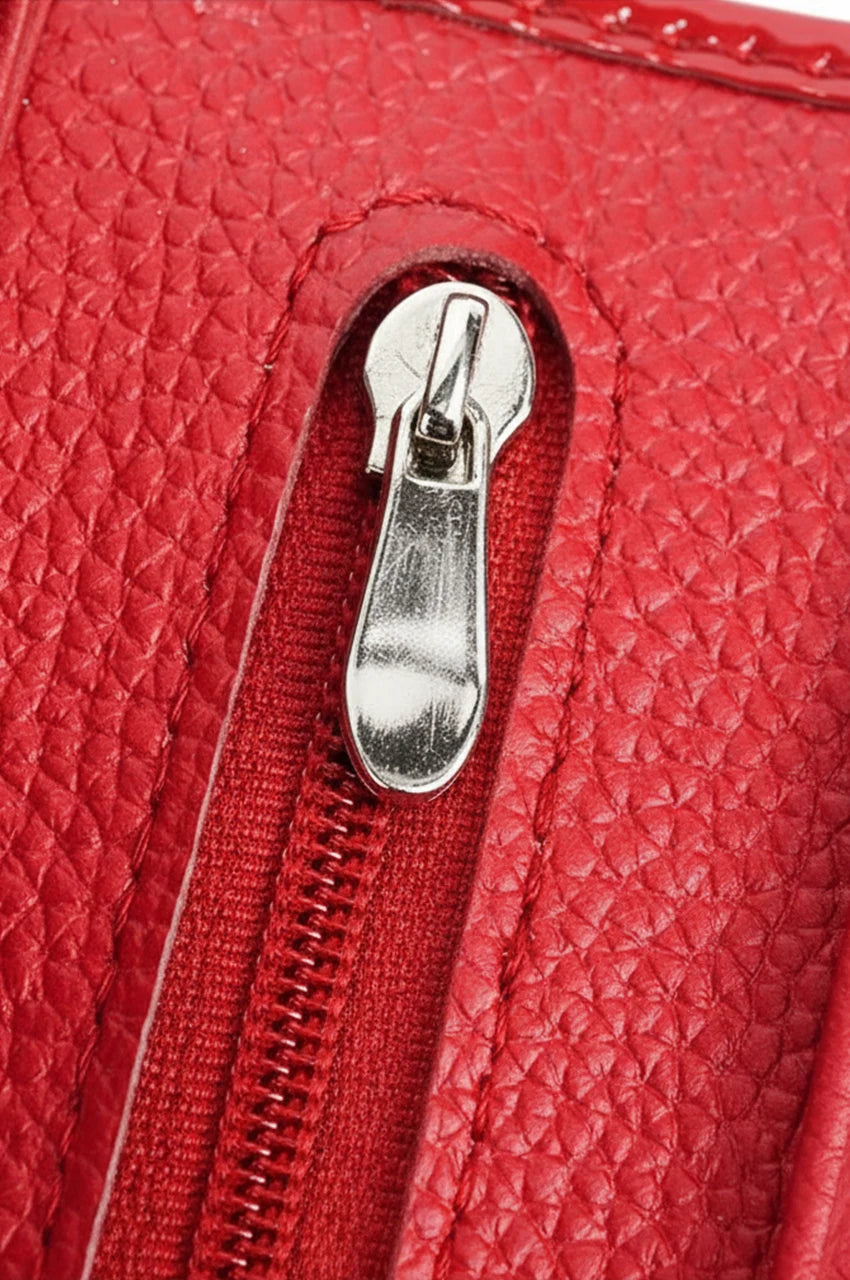 Macro detail of the red patent wallet's zipper pull and textured leather surface.