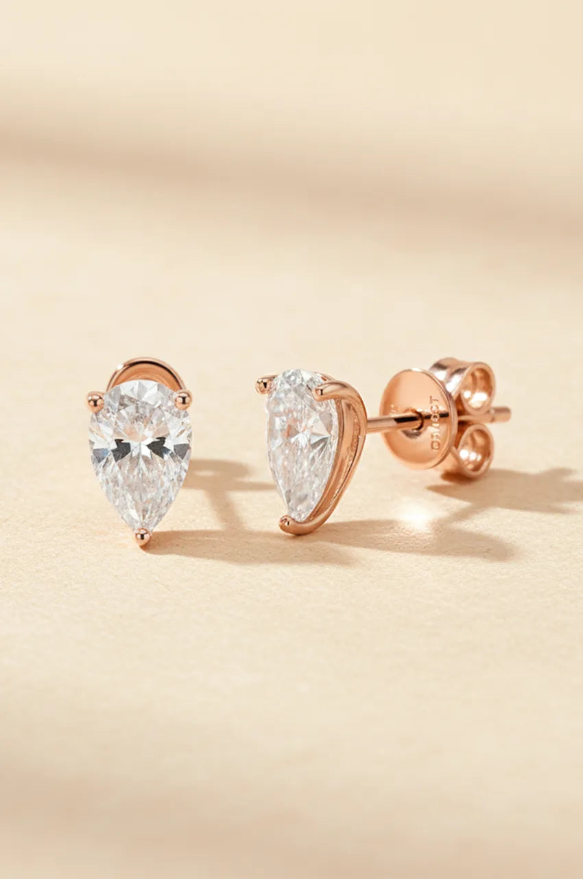 Front facing view of rose gold pear cut studs on a beige background.