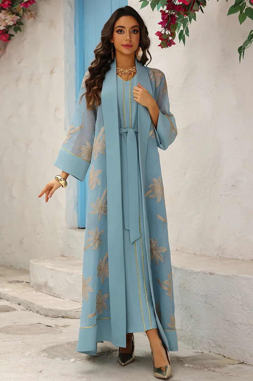 Detail view of the wide-cut sleeves and gold piping on the SAELA light blue palm tree kaftan.