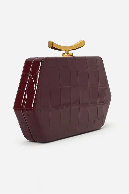 Side profile of geometric burgundy evening bag showing depth, patent finish, and gold top clasp.