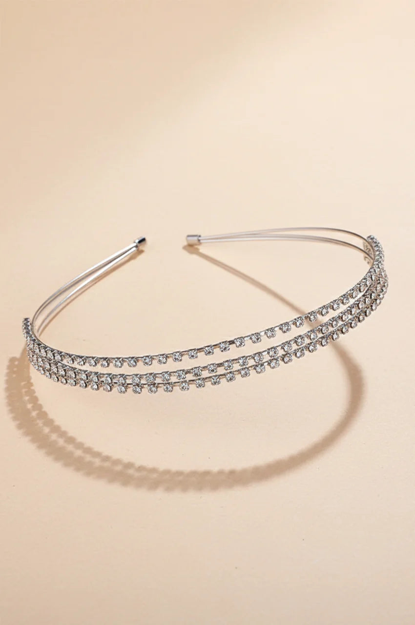 Front view of minimalist silver double-row rhinestone headband on beige background.