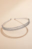 Front view of minimalist silver double-row rhinestone headband on beige background.