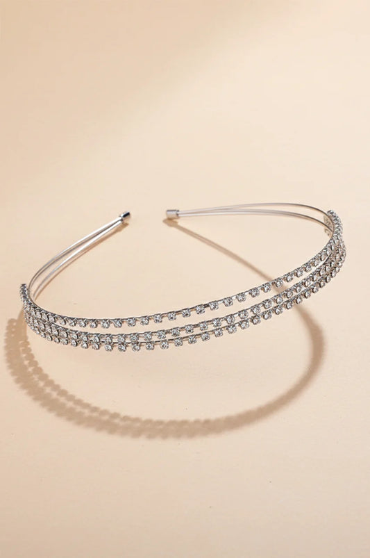 Front view of minimalist silver double-row rhinestone headband on beige background.