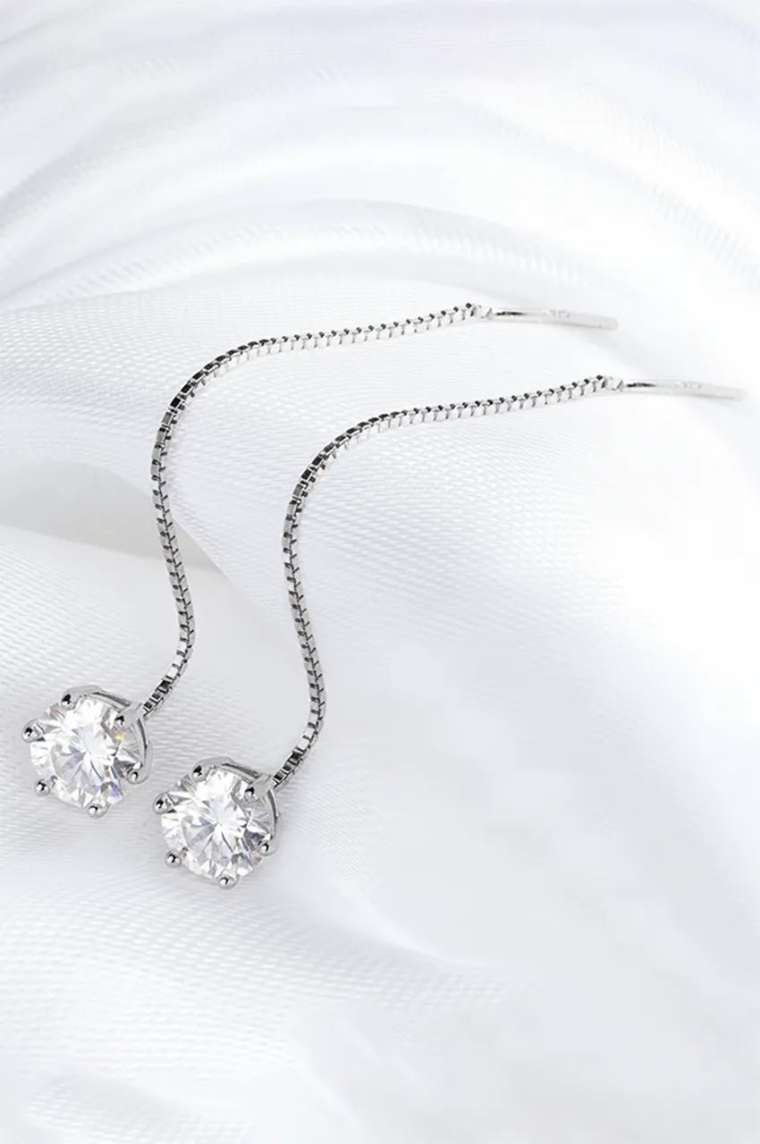 Pair of sterling silver long drop chain earrings with moissanite stones resting on white fabric.