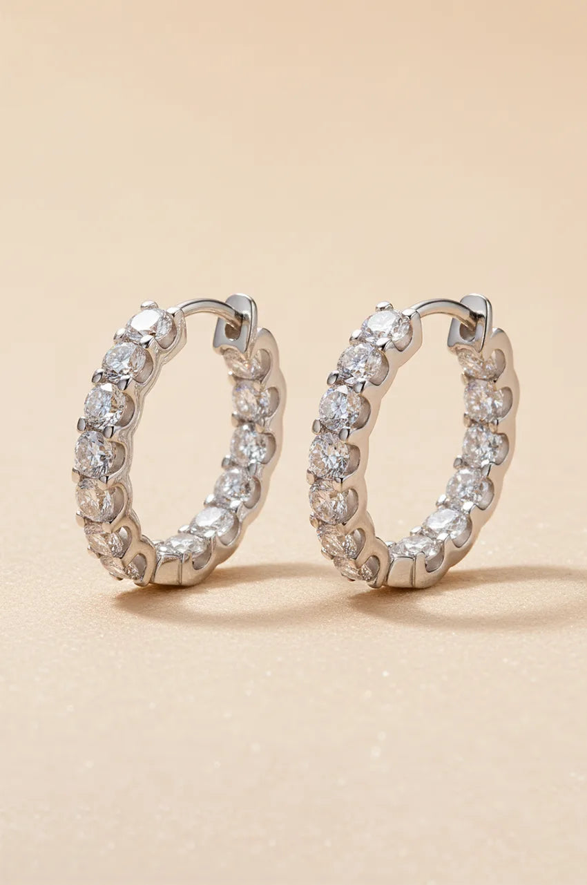 Front view of sterling silver huggie hoop earrings paved with moissanite stones on beige background.
