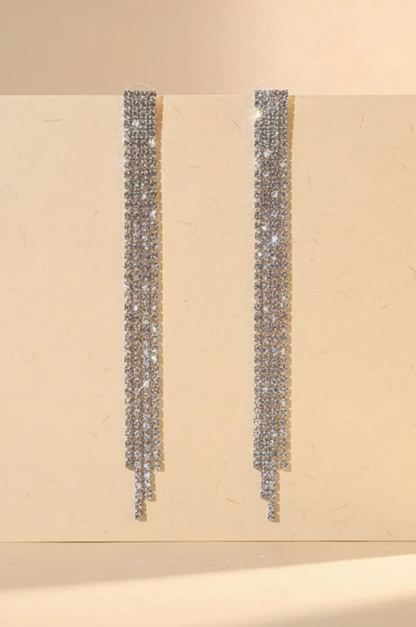 Front view of long silver rhinestone tassel earrings hanging against a beige background.