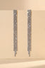 Front view of long silver rhinestone tassel earrings hanging against a beige background.