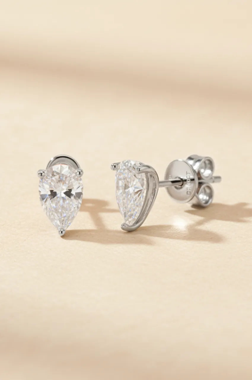 Front view of silver pear-shaped diamond simulant earrings on beige texture.