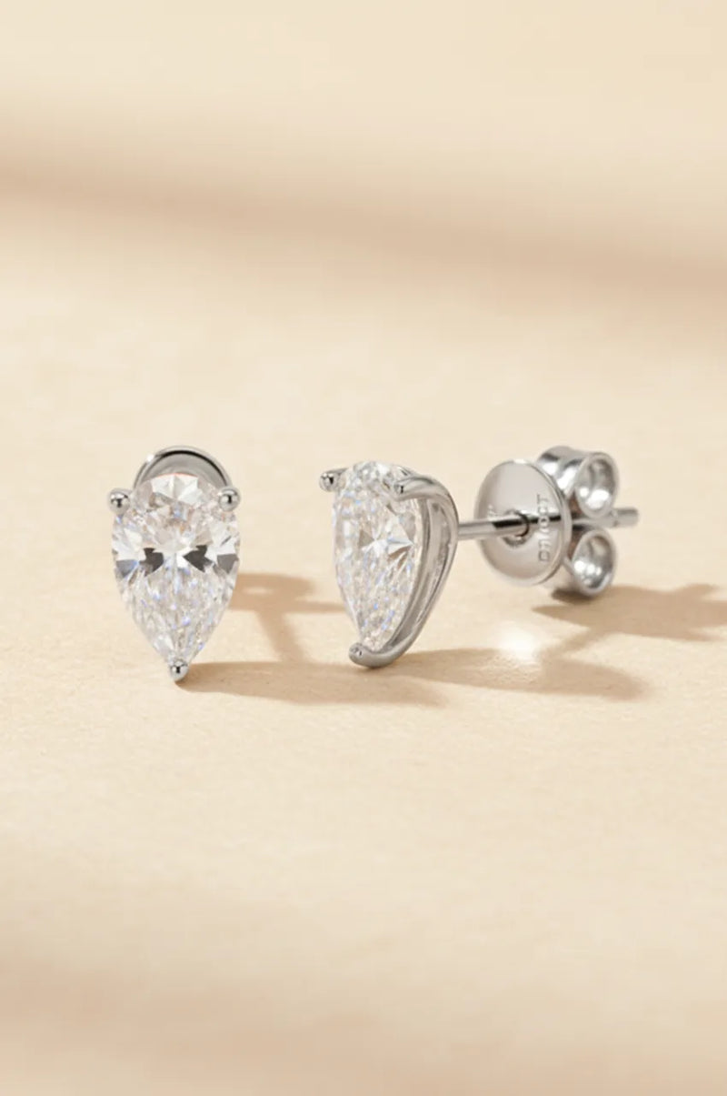 Front view of silver pear-shaped diamond simulant earrings on beige texture.