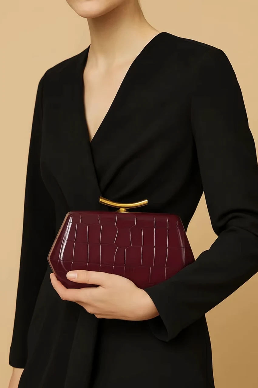 Model wearing a black v-neck top holding a deep red geometric clutch with a gold sculptural handle.