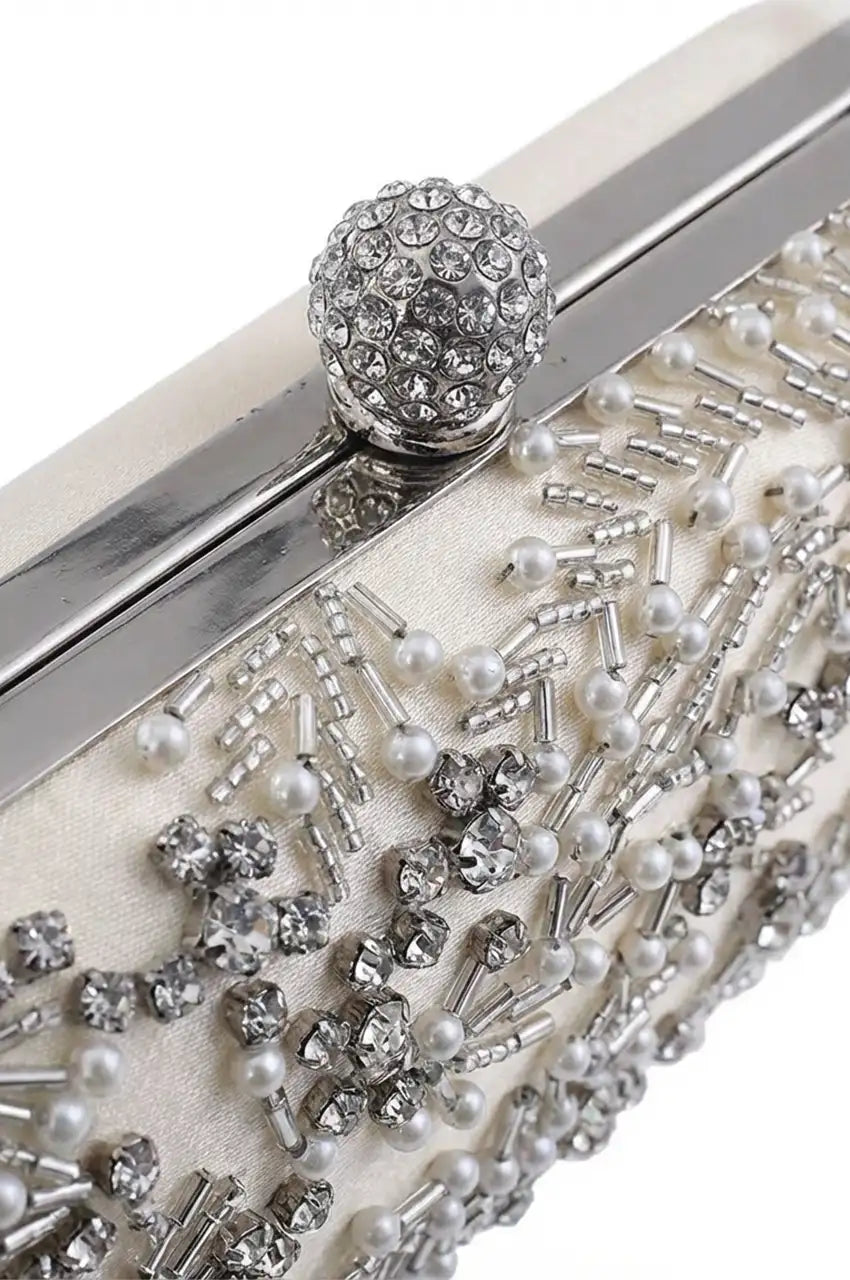 Close-up detail of the sparkling rhinestone-encrusted ball clasp and silver metal frame on the white satin clutch.