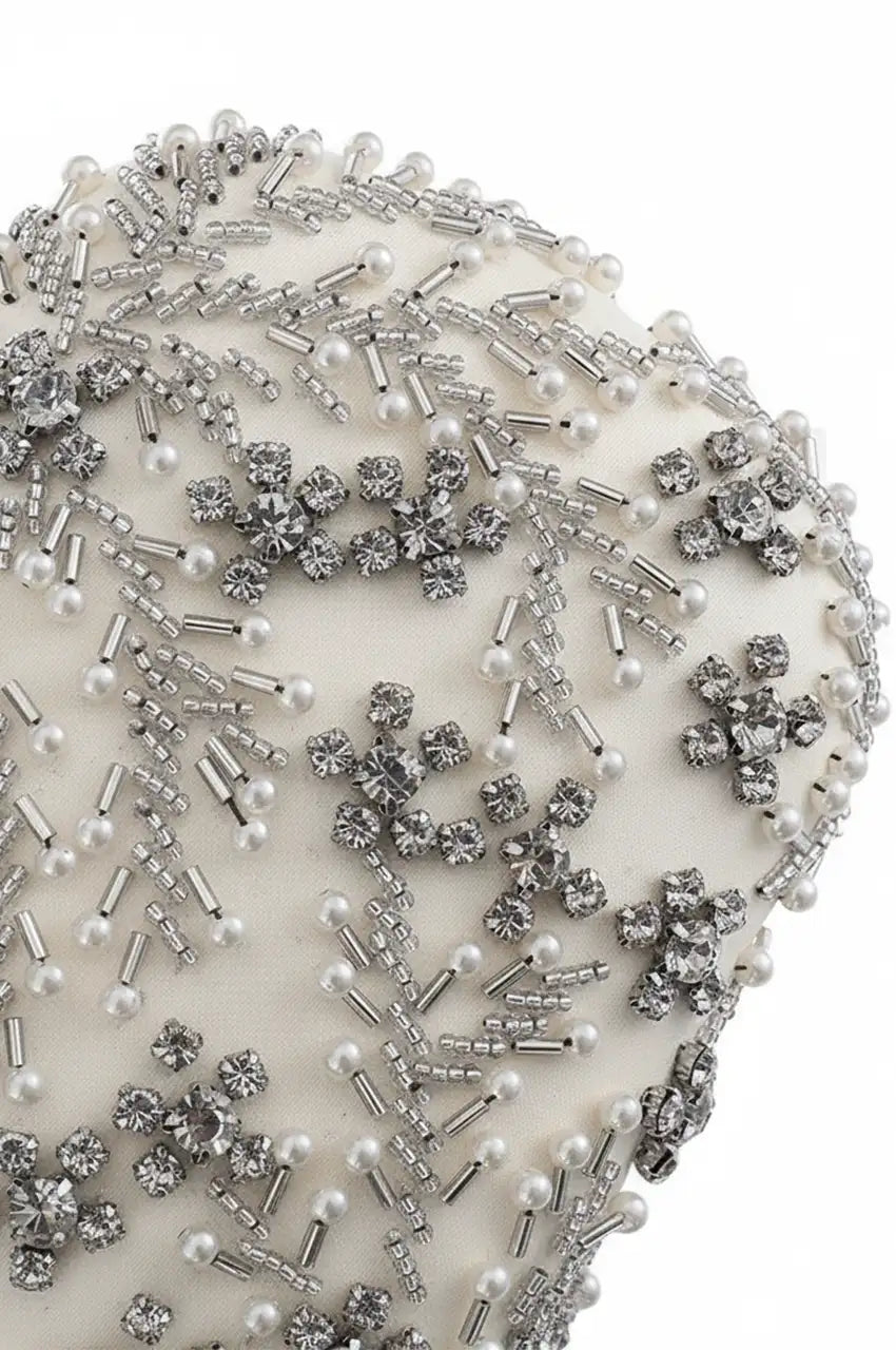 Macro close-up detail of white satin texture embellished with hand-beaded faux pearls, silver tubes, and clear crystals.